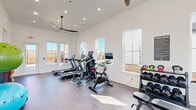 Located at 202 Ryan Rd in Pea Ridge, Arkansas, this fitness center is a thoughtfully designed exercise space that offers a comprehensive workout environment within a single, open room. The space is defined by its soaring vaulted ceilings, crisp white walls, and wide-plank hardwood-style flooring, creating a clean and energizing atmosphere throughout.

Natural light pours in through multiple large windows positioned along the walls, providing views of the surrounding exterior and keeping the space feeling open and airy. Two ceiling fans with wide, modern blades provide additional airflow and comfort during workouts. Recessed lighting supplements the natural illumination for consistent brightness at all times of day.

The fitness center is equipped with a strong lineup of cardio equipment, including multiple Bodycraft treadmills, an elliptical trainer, and a spin bike with an integrated screen. A dedicated strength training area features a multi-function cable machine, an adjustable weight bench, a full rack of dumbbells, and a colorful set of kettlebells. Stability and flexibility training is also supported through stability balls and additional accessories. A glass exterior door provides convenient direct access to the outdoors. The space is managed with posted fitness center guidelines, reflecting a well-maintained and organized facility.