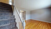 Located at 3 Colonial Ct in Plainville, Connecticut, this three-floor home offers a well-organized layout with consistent design elements throughout. The main level welcomes visitors through a front entry door with sidelights, opening into a bright living area finished with gleaming hardwood floors and cool-toned gray walls. Natural light filters in through windows fitted with blinds, complemented by baseboard heating along the walls. A carpeted staircase with a classic white-painted balustrade and newel post connects the floors, adding a traditional architectural touch.

The kitchen is equipped with warm oak cabinetry, dark granite-style countertops, a tiled backsplash, and standard appliances including a refrigerator and dishwasher. A peninsula provides additional counter space, and a sliding glass door opens directly to the outdoors, allowing natural light to flow into the space.

The upper level continues the hardwood flooring theme across generously sized bedrooms, each featuring neutral gray walls, windows with natural light, and baseboard heating. A full bathroom on this level includes a tub/shower combination with white tile surround, a single vanity, and tile flooring.

The lower level presents an unfinished basement with painted concrete walls, a concrete floor, and exposed wooden ceiling joists, offering substantial potential for storage or future customization.