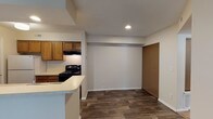 Located at 1956 Chimney Ln in Kettering, Ohio, this single-floor residence offers a functional and well-organized layout designed for comfortable everyday living. The kitchen is a standout feature, equipped with warm oak cabinetry, light countertops, a double-basin sink, a black gas range, a dishwasher, and a full-size refrigerator. A peninsula counter seamlessly connects the kitchen to the adjacent living area, creating an open and accessible flow between spaces. Wood-look plank flooring runs throughout the kitchen and main living areas, providing a durable and cohesive aesthetic. The living area is enhanced by a fireplace, adding a welcoming focal point to the space. Multiple bedrooms are finished with soft wall-to-wall carpeting and feature windows that allow natural light and views of the surrounding greenery. The bathroom is appointed with a warm wood vanity, light countertop, a large mirror with overhead lighting, and matching wood-look flooring. Neutral wall tones and textured ceilings are consistent throughout the home, contributing to a clean and understated interior. The layout, as seen in the dollhouse view, provides a logical and connected flow from the entryway through the living, kitchen, and private bedroom areas.