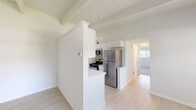 This single-floor residence combines functional design with a clean, airy aesthetic throughout its well-organized layout. The kitchen is a standout feature, designed in a galley configuration with white shaker cabinetry extending to the ceiling, a gray subway tile backsplash, light stone countertops, a single-basin sink with a brushed gold faucet, and a full suite of stainless steel appliances including a gas range, microwave, and refrigerator. A half-wall peninsula separates the kitchen from the adjacent living area, enhancing the open feel of the space. Exposed painted beams run across the tongue-and-groove ceiling, adding architectural character that carries through the main living areas. The bedrooms are carpeted and feature large windows that invite natural light and offer views of surrounding greenery. Each bedroom includes closet storage, with at least one room offering a built-in closet with a hanging rod. The bathroom is finished with a white tub-shower combination and brushed nickel hardware. Light wood-tone flooring runs through the common areas, complementing the all-white walls and trim. The overall atmosphere is bright, neutral, and move-in ready, with thoughtful details that balance practicality and style.