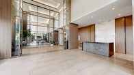 The amenity spaces at HARMONI in Montréal, QC present a refined and upscale environment designed to elevate everyday living. The grand entrance lobby immediately sets the tone with soaring double-height ceilings, floor-to-ceiling glass partitions framed in brushed gold, and expansive large-format porcelain tile flooring in warm cream tones. A sleek stone reception desk anchors the space, while carefully placed seating areas and lush greenery create a welcoming, hotel-inspired atmosphere. Natural light pours in generously through the sweeping glazed façade, offering views of the surrounding grounds. Beyond the lobby, corridors finished with the same polished tile lead residents through to the building's wellness facilities. The indoor swimming pool is a standout feature, boasting luminous turquoise water beneath a high reflective ceiling and surrounded by comfortable lounge seating. Large windows and glass doors open directly to an outdoor terrace, seamlessly blending indoor and outdoor relaxation. The fitness centre is well-appointed with a full suite of cardio and strength equipment, mirrored walls, and large windows that bring in abundant natural light. The warm wood accents and gold-toned architectural details seen throughout the lobby carry cohesively into adjoining spaces, lending the entire amenity floor a consistent sense of contemporary elegance.