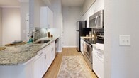 This 940-square-foot, single-story apartment at 2054 Riverside Avenue in Jacksonville, FL offers a well-designed 2-bedroom, 2-bathroom layout with consistent wood-look flooring throughout. The spacious living room features crown molding, a ceiling fan, track lighting, and French doors that invite natural light and outdoor views. The galley-style kitchen is outfitted with white shaker cabinetry, granite countertops, a grey subway tile backsplash, stainless steel appliances including a refrigerator, range, microwave, and dishwasher, and a stainless steel sink. Both bedrooms include ceiling fans and generous walk-in closets equipped with wire shelving systems. The primary bedroom spans 150 square feet and offers windows with exterior views. Each bathroom features white shaker vanity cabinetry, granite countertops, large mirrors, and wood-look flooring. The layout also includes a hallway connecting the main living areas to the bedrooms. Neutral-toned walls and light flooring create a bright, cohesive aesthetic throughout this functional and efficiently organized apartment.