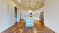 This single-floor residence located along US-19 S in Alpharetta, Georgia, offers a well-designed layout with a bright, cohesive aesthetic throughout. The kitchen serves as a central highlight, showcasing white shaker cabinetry, light quartz countertops, and a distinctive blue hexagonal tile backsplash. Stainless steel appliances, including a range, built-in microwave, and refrigerator, complement the space, while a freestanding island with open shelving provides additional workspace and storage. Warm herringbone-patterned hardwood flooring extends throughout the kitchen and main living areas, accented by crown molding and recessed and pendant lighting with gold-toned fixtures.

The bedrooms feature plush neutral carpeting and are generously proportioned, with one bedroom benefiting from large windows that invite natural light and outdoor views. Each bedroom is accompanied by a walk-in closet outfitted with multi-tiered wire shelving systems, offering practical and abundant storage.

The bathroom presents a refined finish with large-format marble-look tile covering both the floors and shower surround, paired with a soaking tub. An in-unit laundry area is also visible, adding everyday convenience. Overall, the space delivers a clean, modern feel with quality finishes throughout.