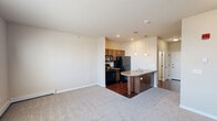 Located at 3709 7th St W in Williston, North Dakota, this efficiently designed single-floor unit offers a thoughtful layout that maximizes every square foot. The open-concept living and kitchen area serves as the heart of the space, where rich hardwood-style flooring transitions seamlessly into plush carpeting in the living area. The kitchen is well-equipped with dark cabinetry, black appliances including a refrigerator, electric range, and over-the-range microwave, complemented by a peninsula with a double stainless steel sink and stone-toned countertops. Elegant pendant lighting hangs above the peninsula, adding a stylish focal point to the space. A hallway connects the main living area to the private quarters, providing access to the full bathroom, which features a dark wood vanity with stone countertop, a large mirror with vanity lighting, and hardwood-style flooring. The dedicated in-unit laundry area accommodates a full-sized washer and dryer side by side, complete with overhead wire shelving for added storage. Two closets offer ample organization options throughout the unit. A bedroom at the end of the hallway benefits from a large window that invites natural light, creating a bright and comfortable retreat.