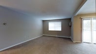 This single-floor residential unit presents a well-organized layout designed for comfortable everyday living. The floor plan reveals a generous open living area that serves as the central hub of the space, finished with wall-to-wall carpeting in a neutral tone that adds warmth underfoot. A large window fitted with blinds allows natural light to fill the room, complemented by baseboard heating that runs along the perimeter walls, ensuring year-round comfort. The neutral, taupe-toned walls throughout provide a clean and versatile backdrop. Adjacent to the living area, the kitchen is clearly defined and equipped with standard cabinetry and appliances, offering a practical cooking and preparation space. A dedicated bathroom is visible within the floor plan, thoughtfully positioned for easy access from the main living zones. Additional rooms branch off from the central corridor, providing flexible spaces suitable for use as bedrooms or home offices. The overall layout is efficient and logical, with well-proportioned rooms that flow naturally from one to the next. The consistent color palette and straightforward finishes throughout give the space a cohesive, move-in-ready character ideal for a range of occupants.
