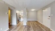 This single-floor residence offers a thoughtfully designed layout that balances modern finishes with practical functionality. The open-concept living area is anchored by warm wood-look vinyl plank flooring and neutral gray walls, creating a bright and welcoming atmosphere throughout the main living spaces.

The kitchen is a standout feature, boasting crisp white shaker-style cabinetry, gray quartz countertops, and a classic white subway tile backsplash. A full suite of stainless steel appliances — including a gas range, refrigerator, built-in microwave, and dishwasher — is complemented by a gold-finish faucet, adding a contemporary touch. The kitchen connects seamlessly to the living area via a partially open wall with a structural column, enhancing the sense of flow.

The bedroom features plush wall-to-wall carpeting and is serviced by a generously sized walk-in closet outfitted with wire shelving systems on multiple walls, providing ample storage. An additional door from the main hallway offers convenient access.

The bathroom is designed with accessibility in mind, featuring a walk-in soaking tub with a built-in seat, sturdy grab bars throughout, white tile surround, a single-sink vanity with quartz countertop, and a mirror. White clean-line cabinetry ties the space together cohesively. Overall, the residence presents a clean, modern aesthetic with practical, inclusive design elements.