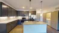 Located at 7770 Market St in Wilmington, NC, this single-floor unit offers a thoughtfully designed, contemporary living space with clean finishes throughout. The open-concept kitchen serves as a focal point, featuring dark gray shaker-style cabinetry extending to the ceiling, stainless steel appliances including a French door refrigerator, electric range, and built-in microwave. A light-toned quartz peninsula with an undermount sink provides additional workspace and casual dining potential, while pendant lighting and a neutral tile backsplash complete the polished aesthetic. Wood-look plank flooring flows seamlessly from the kitchen into the living area, which is bright and open, benefiting from a large window and a sliding door that opens to a private balcony. A ceiling fan adds comfort to this generously sized main area. The bedroom is carpeted for warmth and comfort, featuring a ceiling fan with light fixture and a window that invites natural light. The bathroom is well-finished with a dark vanity, granite-style countertop, large mirror with overhead lighting, and wood-look flooring, connecting directly to the bedroom for convenient access.