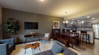 This single-floor residence at 17016 East Indiana Avenue in Spokane Valley offers a thoughtfully designed open-concept layout that connects the living, dining, and kitchen areas into one cohesive, functional space. The living room benefits from large windows that invite generous natural light and outdoor views, complementing the warm, neutral-toned walls and wood-accented flooring found throughout the unit.

The kitchen is well-appointed with dark espresso cabinetry, stainless steel appliances including a range, microwave, and refrigerator, dark countertops, a stone tile backsplash, recessed lighting, and pendant fixtures. It opens directly into the dining area, which comfortably accommodates a full-sized dining table with bench seating, making it well-suited for entertaining.

Two carpeted bedrooms provide comfortable retreats, each offering adequate space for furnishings. The primary bedroom includes access to a dedicated bathroom and closet. A second full bathroom mirrors the contemporary styling found throughout, featuring dark vanity cabinetry, wood-look flooring, and a shower-tub combination. An enclosed laundry area houses a full-sized washer and dryer with overhead shelving for added storage convenience.