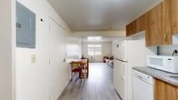 Located at 210 Lake St in Ithaca, NY, this single-floor unit offers three bedrooms and one bathroom within a practical and well-organized layout. The open-concept main area combines a living space and dining area, illuminated by a centrally placed window that brings in natural light. Light gray wood-style flooring runs throughout, providing a cohesive and easy-to-maintain surface across all rooms. The kitchen is equipped with warm wood-toned cabinetry, granite-style countertops, a white electric range, and a full-size refrigerator. A window above the kitchen counter adds additional natural light to the space. The three bedrooms vary in size and character. The primary bedroom is the most spacious of the three, featuring dual windows with neighborhood views and room for a desk and bed. The second bedroom includes a window with outdoor views and a baseboard heating unit, while the third bedroom offers a wood wardrobe and dresser. The shared bathroom features tile flooring, white cabinetry for storage, and clean white walls. Two hallways connect the rooms, ensuring an efficient flow throughout. The unit's clean, neutral palette and consistent flooring create a straightforward and functional living environment suited for multiple occupants.