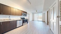 This well-designed single-floor residence offers a clean, contemporary aesthetic throughout, anchored by light-toned hardwood flooring that runs seamlessly across the open living areas. The open-concept layout connects the living space directly to the kitchen, creating a functional and airy floor plan ideal for everyday living and entertaining.

The kitchen is a standout feature, outfitted with rich dark-toned cabinetry, granite-style countertops, a white subway tile backsplash, and a full suite of stainless steel appliances including a refrigerator, range, microwave, and dishwasher. Track lighting overhead ensures excellent task illumination throughout.

The living area is bright and spacious, benefiting from large sliding glass doors fitted with vertical blinds that lead directly to a private balcony, filling the space with natural light and providing outdoor views. A ceiling fan adds both function and style to the area.

The bedrooms are calm and well-lit, each featuring large windows with horizontal blinds that frame outdoor views and allow for ample natural light. Closet storage is thoughtfully integrated into the layout.

The bathroom is finished to a high standard, featuring large-format tile flooring, a tiled soaking tub surround, dark wood vanity cabinetry with granite countertops, and a sizeable mirror. The overall ambiance of the residence is bright, modern, and move-in ready.