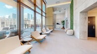 Located at 900 Rue Saint-Jacques in the heart of Montréal, this elegantly designed lounge spans a single, generously proportioned floor, offering an upscale retreat with a distinctly contemporary character. The space is defined by soaring floor-to-ceiling windows framed in warm wood that flood the interior with abundant natural light and deliver sweeping panoramic views of the Montréal skyline.

The lounge is organized into several distinct seating areas, each thoughtfully curated to encourage relaxation and social interaction. One zone features teak-framed chaise lounges with crisp white cushions alongside rounded terracotta-toned side tables, creating a resort-inspired atmosphere. A separate lounge area offers plush barrel chairs in navy blue and blush tones arranged around dark wood coffee tables atop an artful area rug, adding warmth and texture to the light tile flooring.

Architectural contrast is achieved through the juxtaposition of raw exposed concrete walls and refined warm wood paneling, lending the space both industrial character and organic warmth. A living moss wall introduces a vibrant natural element, complemented by potted indoor plants placed throughout. Recessed lighting and pendant fixtures provide ambient illumination, while direct access to an outdoor terrace further extends the lounge experience. The overall ambiance is one of calm sophistication, well-suited for both quiet relaxation and curated social gatherings.