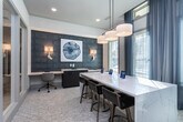 Located at 1879–1881 Riverside Pkwy in Douglasville, Georgia, this single-floor professional office space combines refined aesthetics with highly functional design. The welcoming reception area anchors the space with a striking marble-top counter featuring elegant white veining, pendant drum lighting overhead, and patterned carpeting that extends throughout the main corridors.

A series of private offices line the hallway, each enclosed with full-height glass-paneled partitions and framed glass doors that allow natural light to flow through the space while maintaining acoustic privacy. Each office is thoughtfully appointed, with one featuring a dramatic dark wood-paneled accent wall, wall-mounted sconce lighting, built-in white countertop workstations, and curated wall art, creating a sophisticated yet productive environment.

A collaborative workstation area offers a large marble-surface table surrounded by modern seating, bathed in natural light from multiple large windows dressed with sheer draping curtains and wood blinds. Pendant cluster lighting illuminates this gathering space, making it ideal for meetings or shared work sessions.

The corridor connecting the offices is bright and open, with consistent flooring, clean white walls, and an organized layout that promotes easy navigation throughout the suite. Overall, the space strikes a balance between professional polish and welcoming warmth.
