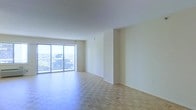 This single-floor space offers a clean, open layout characterized by an abundance of natural light and a neutral color palette throughout. The main living area is finished with warm parquet hardwood flooring laid in a classic herringbone-style pattern, adding visual texture and a timeless quality to the space. Smooth white ceilings complement the light-toned walls, contributing to a bright and airy ambiance.

A prominent feature of the space is the large sliding glass door that spans a significant portion of one wall, flooding the interior with natural light and providing direct access to a private balcony. The balcony offers elevated, panoramic views of the surrounding landscape, making it a standout element of the space. The generous proportions of the main living area allow for flexible furniture arrangements to suit various needs.

The overall design is understated and versatile, with minimal architectural detailing that allows the natural light and outdoor views to take center stage. The open flow and neutral finishes provide a solid foundation for a variety of interior design styles.