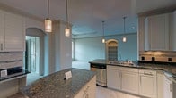 Located within the Bexley Lake Forest community in Richardson, TX, this single-floor residence offers a thoughtfully designed open layout. The kitchen is a standout feature, equipped with white cabinetry, stainless steel appliances including a refrigerator, range, microwave, and dishwasher, along with rich dark granite countertops, a stone tile backsplash, and a curved peninsula island. Pendant lighting and track lighting illuminate the space, while large-format tile flooring adds a clean, polished look. The kitchen opens directly into the living area, which features a tray ceiling with crown molding and plush carpeting. A full-height door with sidelights allows natural light to flow in and provides views to the outdoors. The bedrooms are carpeted and bright, each offering multiple windows with blinds. One bedroom includes a ceiling fan and a closet with built-in shelving. The bathrooms are finished with granite-topped vanities, tiled tub-shower combinations with curved curtain rods, and tile flooring. A built-in arched shelving nook adds a decorative architectural touch to the main living area, enhancing the overall character of this well-appointed single-level home.