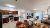 This thoughtfully designed one-bedroom, one-bathroom residence offers a functional and stylish layout across a single floor. The open-concept kitchen and living area serves as the heart of the home, seamlessly blending cooking, dining, and relaxing spaces. The kitchen is equipped with rich, warm-toned cabinetry, stainless steel appliances including a range, microwave, and refrigerator, and granite-style countertops that extend to a peninsula with bar seating. Light wood-style flooring flows through the kitchen and dining area, contributing to a clean, modern aesthetic.

The living room is generously proportioned with plush carpet, crown molding, and a bold accent wall in a deep slate blue that lends character and depth to the space. A sliding glass door floods the room with natural light and provides outdoor access. The bedroom is a comfortable retreat, featuring carpet flooring, a natural light-filled window with patterned drapes, and a dedicated closet. The full bathroom is finished with granite countertops, warm wood cabinetry, a large mirror, and a tub-shower combination. Throughout the residence, crisp white walls and consistent finishes create a cohesive and inviting atmosphere.