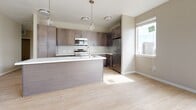 This single-floor residence features three bedrooms and one bathroom across a thoughtfully designed floor plan. The living area is bright and open, finished with light-toned hardwood flooring, neutral warm-beige walls, and multiple windows that invite natural light throughout the day. A white exterior door adds a clean, welcoming touch to the space.

The kitchen is a standout feature, showcasing contemporary dark wood cabinetry that extends to the ceiling for generous storage, complemented by a white subway tile backsplash and crisp white countertops. A large central island with pendant lighting overhead serves as both a prep area and casual gathering spot. Stainless steel appliances, including a refrigerator, range, and over-the-range microwave, complete the modern kitchen ensemble. The hardwood flooring continues seamlessly from the living area into the kitchen.

Each of the three bedrooms is finished with plush neutral carpeting and painted in soft, warm tones. The bedrooms receive natural light through double-hung windows, with views of the surrounding neighborhood. One bedroom includes a ceiling fan for added comfort. The overall ambiance of this residence is clean, modern, and move-in ready, with a cohesive neutral palette that provides a versatile backdrop for any décor style.