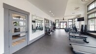 The Wynfield fitness center at 2549 S George St in York, PA is a thoughtfully designed, single-floor facility offering a comprehensive workout environment. The space is divided into distinct functional zones, each tailored to specific training needs. The main area features soaring ceilings with clerestory windows that flood the interior with natural light, complemented by modern ring-style pendant lighting and recessed fixtures that maintain a bright, energizing atmosphere.

The cardio section is well-equipped with multiple treadmills, elliptical trainers, and stationary bikes, all positioned near large, gray-trimmed windows overlooking the surrounding community. A dedicated free weights area includes a full dumbbell rack and flat benches, situated alongside floor-to-ceiling mirrors that enhance the sense of space. A functional training zone provides a cable machine and resistance equipment, along with medicine balls and stability tools for varied workouts.

Throughout the facility, dark rubberized flooring provides durability and safety, while ceiling fans ensure comfort during intense sessions. Wall-mounted televisions are strategically placed for entertainment. Glass-paneled doors with a Wynfield-branded entry mat offer a polished, welcoming entrance, reinforcing the facility's clean, contemporary aesthetic.