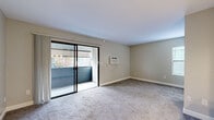 This efficiently designed unit on Carroll Canyon Road makes thoughtful use of its compact footprint, offering a living room, kitchen, full bathroom, and closet across a single floor. The living room serves as the central gathering space, finished with plush gray carpeting and neutral beige walls that create a clean, understated atmosphere. A wall-mounted HVAC unit provides climate control, while sliding glass doors open directly onto a private balcony, bringing in natural light and views of surrounding greenery. The kitchen is well-appointed with white shaker-style cabinetry extending to the ceiling for ample storage, light wood-look vinyl flooring, a stainless steel range and microwave, a single-basin sink, and a light-colored countertop that extends into a peninsula. The entry area adjacent to the kitchen features additional cabinetry and a secure front door with a keypad. The bathroom is finished in a bright, all-white palette with light wood-look flooring, a single-sink vanity with white cabinetry, a wall-mounted mirror with overhead lighting, and a full soaking tub with shower. Clean lines and a consistent neutral color scheme unify the space throughout.