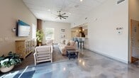 Located at 1500 Lewis Turner Blvd. in Fort Walton Beach, FL, this single-floor community amenity space offers a well-rounded selection of recreational and social areas designed for comfort and activity. The layout flows across several distinct zones, each serving a specific purpose while maintaining a cohesive, clean aesthetic throughout.

The fitness center is a standout feature, energized by bold red and teal accent walls, rubber flooring, and large windows that bring in natural light. It is outfitted with treadmills, ellipticals, a rowing machine, cable machines, free weights, and wall-mounted mirrors, providing a comprehensive workout environment.

Adjacent to the fitness area is a game room centered around a full-size billiards table with a bright teal felt surface, complemented by bar-height seating and wall art. Polished concrete floors run through much of the space, lending a modern industrial character.

The living room areas feature comfortable seating arrangements, wall-mounted televisions, decorative storage consoles, and potted plants that add warmth. Exposed brick columns provide architectural charm, while large windows offer views of the surrounding greenery.

The kitchen is well-appointed with dark shaker-style cabinetry, granite countertops, stainless steel appliances including a full-size refrigerator and microwave, and a double-basin sink beneath a bright window. A small dining area with a round table and chairs completes the social space.