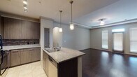 This single-floor residence is designed with a modern, open-concept layout that seamlessly connects the kitchen and living areas. The kitchen is a standout feature, anchored by a central island with granite countertops and a stainless steel sink illuminated by two pendant lights. Dark espresso cabinetry lines the walls, complemented by a tile backsplash, granite counters along the perimeter, and stainless steel appliances including a refrigerator, microwave, and range. Light ceramic tile flooring grounds the kitchen space.

The open living area transitions to rich, dark hardwood floors and is defined by a tray ceiling with crown molding and a ceiling fan. Windows fitted with blinds allow natural light to filter into the space, enhancing its airy feel.

The bedrooms feature neutral carpet and receive natural light through blinds-covered windows. Both bathrooms are finished consistently, each offering a tub and shower combination with white subway tile surround, a granite-topped vanity with dark cabinetry, a large mirror, and light tile flooring. The overall aesthetic throughout is cohesive, contemporary, and understated.