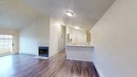 Located at 7002 N Colton St in Spokane, WA, this single-floor residence offers a well-organized layout with consistent hardwood-style flooring running throughout. The open living area is a focal point of the home, featuring vaulted ceilings that lend a sense of spaciousness and a tile-surround wood-burning fireplace that serves as a functional centerpiece. Baseboard heating units are present throughout, providing reliable warmth during Spokane winters.

The kitchen is designed with an open-concept peninsula that extends into the living space, offering a stainless steel sink, white coil-top range, white refrigerator, and light wood cabinetry with ample upper storage. The layout allows for easy interaction between kitchen and living areas.

The bedrooms feature the same hardwood-style flooring, vaulted or angled ceilings, and windows that bring in natural light. Each room provides a clean, neutral palette with white walls and trim. The bathroom includes a single-sink vanity with a large mirror, a tub-shower combination, and a textured ceiling.

A dedicated laundry room houses a full-size washer and dryer alongside a water heater, adding practical convenience to the home's functional design.