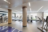 Located at 1000 Ellis Drive in Glen Mills, PA, this professionally designed fitness center offers a generous single-floor layout that accommodates a comprehensive range of workout experiences. The space is anchored by distinctive fluted wood-wrapped columns that add a warm, contemporary aesthetic against the clean white walls and tray ceilings with recessed and linear LED lighting throughout.

The main cardio zone features a row of treadmills and elliptical machines equipped with individual display screens, all positioned to take advantage of large windows that bring in abundant natural light and views of the surrounding greenery. A dedicated strength training area houses a variety of cable and resistance machines, while a free weight section offers a full dumbbell rack alongside flat benches and floor-to-ceiling mirrors that enhance the sense of openness.

A separate functional training area provides space for versatile workouts, including a punching bag and stability ball for dynamic exercise. Decorative motivational artwork punctuates the teal accent walls, contributing to an energizing atmosphere. Durable rubber flooring throughout ensures safety and comfort across all zones. The overall design balances functionality with modern, upscale aesthetics, creating an inviting and well-equipped environment for a full spectrum of fitness activities.