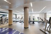 Located at 1000 Ellis Drive in Glen Mills, PA, this professionally designed fitness center offers a generous single-floor layout that accommodates a comprehensive range of workout experiences. The space is anchored by distinctive fluted wood-wrapped columns that add a warm, contemporary aesthetic against the clean white walls and tray ceilings with recessed and linear LED lighting throughout.

The main cardio zone features a row of treadmills and elliptical machines equipped with individual display screens, all positioned to take advantage of large windows that bring in abundant natural light and views of the surrounding greenery. A dedicated strength training area houses a variety of cable and resistance machines, while a free weight section offers a full dumbbell rack alongside flat benches and floor-to-ceiling mirrors that enhance the sense of openness.

A separate functional training area provides space for versatile workouts, including a punching bag and stability ball for dynamic exercise. Decorative motivational artwork punctuates the teal accent walls, contributing to an energizing atmosphere. Durable rubber flooring throughout ensures safety and comfort across all zones. The overall design balances functionality with modern, upscale aesthetics, creating an inviting and well-equipped environment for a full spectrum of fitness activities.