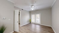 Located at 1640 N Zaragoza Rd in El Paso, TX, this single-story, one-bedroom, two-bathroom home offers a well-designed layout with a clean, neutral aesthetic throughout. Wood-look flooring flows through the main living areas, complemented by crisp white trim and soft gray walls that create a bright, cohesive atmosphere. The living area features crown molding, a ceiling fan, and French doors that invite natural light and outdoor views. The adjacent dining area is accented by an elegant multi-light chandelier and crown molding, adding a polished touch near the entryway. The galley-style kitchen is outfitted with white cabinetry, granite-look countertops, and black appliances, including a range and dishwasher, providing practical functionality. A dedicated laundry room houses a full-size washer and dryer. Both bathrooms feature wood-look flooring, white tile surrounds, and clean, simple vanities. The carpeted bedroom is a comfortable retreat with a ceiling fan, a large window offering natural light, and direct access to a spacious walk-in closet equipped with wire shelving for generous storage. This home offers a practical and comfortable living experience in a functional, well-finished space.