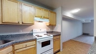 This single-floor residence offers two bedrooms and two bathrooms within a practical, well-organized layout. The kitchen is equipped with light wood cabinetry, granite-style countertops, and white appliances including a coil-top range, refrigerator, and dishwasher. A ventilation hood above the range and ample upper and lower cabinet storage contribute to the kitchen's functionality. Light hardwood-style flooring runs through the kitchen, transitioning into the living area where neutral-toned carpet creates a comfortable atmosphere. The living room benefits from a sliding glass door with vertical blinds that opens to a balcony, allowing natural light to fill the space. Both bedrooms feature plush carpeting, neutral wall tones, and closets with bifold doors for storage. Windows fitted with vertical blinds provide natural light. The two bathrooms are finished with wood-style flooring, white fixtures, and clean, simple vanities. One bathroom includes a soaking tub with a shower surround, while the other features a separate shower. Overall, the space maintains a clean, neutral aesthetic throughout.