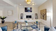 Located at 9200 N Normandale St in Fort Worth, TX, this single-floor space offers a well-designed open-concept layout that seamlessly integrates the kitchen and living areas. The living room is anchored by a white brick fireplace with a mounted television above the mantle, creating a welcoming focal point. Light hardwood-style flooring runs throughout, complementing the neutral, warm color palette of the walls and trim. Large windows along the perimeter flood the space with abundant natural light and provide views of the surrounding outdoor environment, enhancing the bright and airy ambiance. Elegant yellow drum pendant lights add a cheerful pop of color to the ceiling. The kitchen features a peninsula with a light countertop and bar seating, ideal for casual dining or workspace use, alongside stainless steel appliances including a French door refrigerator. A set of French doors with glass panels connects the interior to an adjacent area, adding architectural charm and continuity. The space also includes a dedicated dining nook positioned near the windows, making it a versatile and functional area. Overall, the design balances contemporary style with comfortable, practical living elements throughout.
