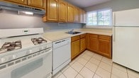 This two-floor, two-bedroom townhouse offers a well-organized layout designed for comfortable everyday living. The main level features a bright living area with durable hardwood-style flooring and a sliding glass door that invites natural light and provides views of the surrounding greenery. A separate dining or secondary living space on this floor also features the same wood-style flooring, complemented by neutral gray walls and baseboard heating. The kitchen is equipped with warm oak cabinetry, ample counter space, a gas range, dishwasher, and a double sink beneath a window — offering both functionality and practicality. Upstairs, the two bedrooms are finished with plush carpeting and neutral tones, creating a calm and restful atmosphere. Each bedroom benefits from natural light via well-placed windows, and baseboard heating ensures year-round comfort. One bedroom features mirrored sliding closet doors, adding a sense of space. The bathroom is finished with tile flooring and tiled shower walls, offering a clean and classic aesthetic. Wall-unit air conditioning is present in select rooms for added climate control. Throughout the home, a consistent gray color palette, white trim, and neutral finishes create a cohesive and move-in-ready environment.
