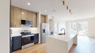 Located in Elkhorn, Nebraska, this thoughtfully designed 2-bedroom, 2-bathroom residence offers a clean, contemporary aesthetic throughout its single-floor layout. The open-concept kitchen serves as the heart of the home, showcasing a generous white quartz island with a matte black faucet and sink, two-tone cabinetry combining navy and warm wood tones, stainless steel appliances, and gold pendant lighting. The kitchen flows seamlessly into the living area, which benefits from large sliding doors that invite abundant natural light and connect the interior to outdoor views. Both bedrooms are carpeted and bright, each featuring wide windows with views of the surrounding neighborhood and ceiling fans for year-round comfort. The primary bedroom is a well-proportioned retreat with access to a dedicated bathroom, complete with a dark-cabinetry vanity, a backlit mirror, and hardwood-style flooring. A walk-in closet with built-in shelving provides ample storage. The second bathroom mirrors the same modern design language, featuring a tub-shower combo with sleek black hardware and a matching vanity. Crisp white walls and light wood-tone flooring in the common areas create a cohesive, airy ambiance throughout this well-appointed Elkhorn residence.