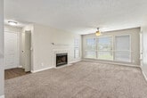 This 1-bedroom, 1-bathroom unit offers a thoughtfully arranged floor plan across a single level. The spacious living room serves as the heart of the home, featuring plush carpeting, a ceiling fan, a tiled wood-burning fireplace with a classic white mantel, and multiple windows fitted with blinds that allow for generous natural light. An entry door leads directly into this bright, open area. The galley-style kitchen is efficiently designed with gray cabinetry, white countertops, hardwood-style flooring, and black appliances including a refrigerator, electric range, and dishwasher — providing ample storage and workspace. The generously sized bedroom features soft carpeting, a ceiling fan with light fixture, and a window that brings in natural light. A louvered door leads to a walk-in closet outfitted with wire shelving and hanging rods, offering substantial storage capacity. The full bathroom includes a tiled shower/tub combo, hardwood-style flooring, a vanity with dark cabinetry, and a well-lit mirror. A hallway connects the main living spaces, completing a cohesive and functional layout throughout.