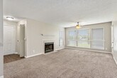 This 1-bedroom, 1-bathroom unit offers a thoughtfully arranged floor plan across a single level. The spacious living room serves as the heart of the home, featuring plush carpeting, a ceiling fan, a tiled wood-burning fireplace with a classic white mantel, and multiple windows fitted with blinds that allow for generous natural light. An entry door leads directly into this bright, open area. The galley-style kitchen is efficiently designed with gray cabinetry, white countertops, hardwood-style flooring, and black appliances including a refrigerator, electric range, and dishwasher — providing ample storage and workspace. The generously sized bedroom features soft carpeting, a ceiling fan with light fixture, and a window that brings in natural light. A louvered door leads to a walk-in closet outfitted with wire shelving and hanging rods, offering substantial storage capacity. The full bathroom includes a tiled shower/tub combo, hardwood-style flooring, a vanity with dark cabinetry, and a well-lit mirror. A hallway connects the main living spaces, completing a cohesive and functional layout throughout.