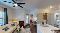 This single-story unit in Houston, TX offers a thoughtfully designed layout that maximizes functionality. The open-concept living area features rich, dark wood-style flooring, a ceiling fan with light fixture, and a private exterior door that allows natural light to filter in through a window. The space flows seamlessly into the kitchen, which is outfitted with dark espresso cabinetry, stainless steel appliances including a refrigerator, range, microwave, and dishwasher, tile backsplash, and a white countertop peninsula that doubles as a breakfast bar.

The bedroom is a comfortable retreat with plush carpet, a ceiling fan, dual windows with blinds and curtain panels, a walk-in closet with built-in shelving, and direct access to the living area. The bathroom features a long vanity with white cabinetry, a wide mirror, bright overhead lighting, wood-style flooring, and a shower-tub combination. An in-unit washer and dryer closet adds everyday convenience. The overall aesthetic is clean and contemporary, with white walls and cohesive finishes throughout.