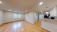 Located at 117 Central St in Acton, Massachusetts, this single-floor unit offers a clean, updated interior with a consistent design aesthetic throughout. Warm-toned hardwood flooring runs continuously across the living areas and bedrooms, lending a cohesive and inviting feel to the entire space.

The open living area is well-lit by recessed lighting and features large multi-pane windows that allow natural light to fill the room, with views of the surrounding neighborhood. Baseboard heating is present throughout, ensuring year-round comfort.

The kitchen is a functional highlight, outfitted with crisp white shaker-style cabinetry, granite countertops, and a full suite of black appliances including a refrigerator, electric range, microwave, and dishwasher. The galley-style layout provides ample counter space and storage, with a clear sightline into the adjacent living areas.

The bathroom features stone tile flooring, a fully tiled tub-and-shower surround with a window, a white vanity with granite countertop, and a medicine cabinet mirror — all contributing to a polished, well-finished feel.

Additional rooms include generously sized bedrooms with multiple windows and recessed or overhead lighting. Interior doors with clean white finishes and neutral wall tones throughout complete the move-in-ready presentation of this well-appointed space.