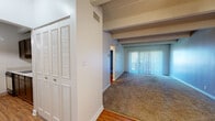 This single-floor residence offers a thoughtfully laid-out living environment defined by a series of distinctive architectural details. A defining feature throughout the space is the exposed beam ceiling with a textured finish, lending a warm, structural character to each room.

The main living area is generously proportioned, featuring plush wall-to-wall carpeting and large sliding glass doors fitted with vertical blinds that invite abundant natural light and provide access to the outdoors. The open sightlines from the entryway through to the living area create a seamless, airy flow. Built-in louvered closet doors near the entry add practical storage while maintaining a clean aesthetic.

The bedroom continues the exposed beam motif and offers a comfortable, carpeted retreat with ample wall space. A ceiling fan ensures year-round comfort.

The kitchen is efficiently designed with dark cabinetry, light countertops, hardwood flooring, and includes a full suite of appliances — refrigerator, oven/range, and dishwasher — providing a functional cooking environment.

The bathroom features classic white subway tile surrounding a full bathtub and shower combination, complemented by safety grab bars and warm hardwood flooring, offering both practicality and clean styling.

Throughout, a consistent palette of neutral tones and natural materials creates a cohesive, welcoming ambiance.
