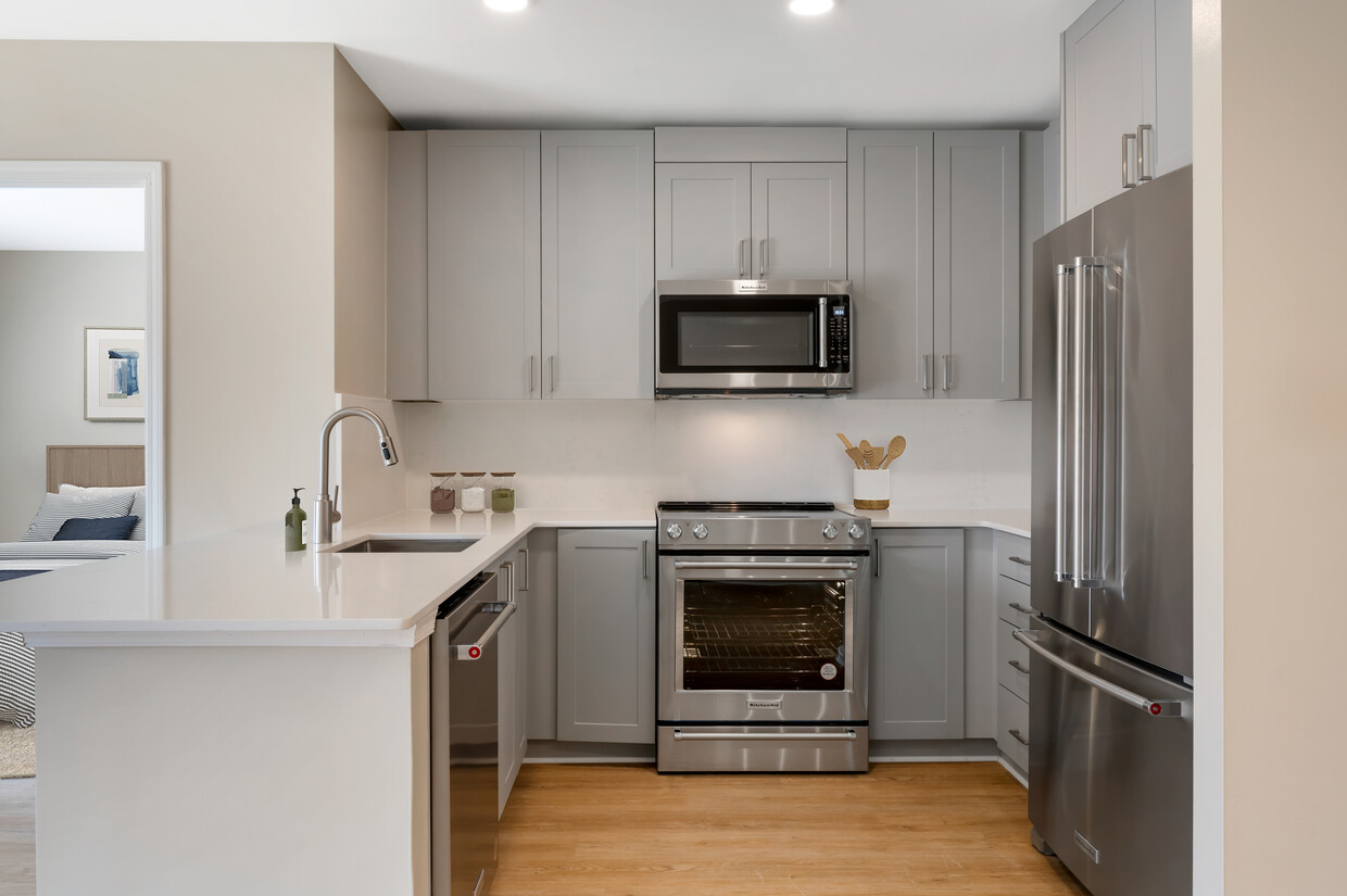 Signature Collection kitchen with grey cabinetry, white marbled quartz countertops and backsplash, stainless steel appliances, and hard surface flooring - Avalon Clarendon