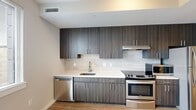 Located at 2811 Telek Place in Alexandria, Virginia, this one-bedroom, one-bathroom unit offers a thoughtfully designed layout across a single floor. The space makes efficient use of every square foot, combining modern finishes with a clean, contemporary aesthetic throughout.

The kitchen is a standout feature, showcasing dark wood-grain cabinetry that extends floor to ceiling, crisp white countertops, a neutral tile backsplash, and a full suite of stainless steel appliances including a gas range and dishwasher. Wood-look plank flooring runs through the main living areas, adding warmth and visual continuity.

The bedroom is a cozy, well-proportioned retreat with neutral walls and plush carpeting, creating a comfortable and quiet environment. A hallway connects the main spaces and leads to the full bathroom, which is finished with large-format light tile flooring, a wood-toned vanity with an integrated sink, a wall mirror, and clean white fixtures.

The unit also includes access to a private outdoor terrace enclosed by concrete block walls — a functional open-air space ideal for fresh air and relaxation. The overall design palette is neutral and modern, with consistent finishes that give the unit a cohesive and move-in-ready feel throughout.
