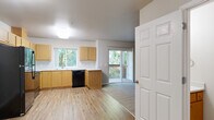 Located at 675 White Oak Cir in Independence, Oregon, this single-floor residence offers a well-organized layout with one bedroom and two full bathrooms. The open kitchen and living area is finished with light wood-style flooring and features light maple cabinetry, black appliances including a refrigerator, range, microwave, and dishwasher, along with light countertops and a window above the sink that brings in natural light with views of surrounding greenery. The living area flows naturally from the kitchen and opens via sliding glass doors to a private wooden deck overlooking mature trees, providing a peaceful outdoor retreat. The bedroom is carpeted and generously proportioned, featuring a sliding closet, a window with outdoor views, and wall heating units for year-round comfort. One bathroom includes a vanity with storage cabinetry and a sliding glass shower enclosure, while the second bathroom offers a tub/shower combination and notably houses in-unit washer and dryer hookups with additional overhead cabinetry — a practical and convenient feature. Throughout the unit, neutral wall tones and consistent flooring materials create a clean, cohesive aesthetic suited to a variety of furnishing styles.