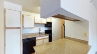 This single-floor unit offers a well-organized layout designed to maximize functionality within a compact footprint. The kitchen serves as a central feature of the space, equipped with black appliances including a dishwasher, electric range, and built-in microwave. White cabinetry with light wood trim lines the upper walls, providing ample storage, while the granite-style countertops add a touch of durability and visual warmth. A peninsula counter extends outward, creating additional prep space and a natural division between the kitchen and the adjoining area, making the layout feel open and connected. The sink is positioned along the counter with a modern faucet, and the overall kitchen design emphasizes practicality. A passthrough view into an adjacent area hints at a refrigerator and additional storage beyond, suggesting a thoughtfully arranged floor plan. The neutral wall tones and light flooring contribute to a clean, understated aesthetic throughout. The unit includes one bedroom and one full bathroom, making it a manageable and efficient living space suited for individuals or couples seeking straightforward, low-maintenance accommodations.