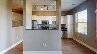 This single-floor residence offers a thoughtfully designed layout that combines modern finishes with functional living spaces. The kitchen serves as a standout feature, showcasing dark granite countertops, crisp white cabinetry, and a full suite of stainless steel appliances including a range, microwave, refrigerator, and dishwasher. A decorative lattice wine rack built into the upper cabinetry adds a distinctive touch, while the soft blue-gray subway tile backsplash provides a refined contrast. Track lighting above the kitchen peninsula illuminates the open-concept cooking and dining area, which flows naturally into the adjoining living spaces. Warm hardwood-style flooring runs throughout the main areas, lending a cohesive and inviting feel, while neutral taupe and gray wall tones create a calm, versatile backdrop. A dedicated room with rich dark hardwood flooring and a double window allows ample natural light to fill the space, making it suitable as a bedroom or home office. The bathroom is finished with matching dark granite countertops, a white undermount sink, white cabinetry with ample storage, a large mirror, and wood-look tile flooring. Grab bars indicate accessibility-conscious design. Together, the consistent finishes and open flow make this a comfortable and practical living space.