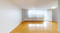 Located at 45 Driftwood Ave in Toronto's north end, this two-bedroom, two-bathroom unit offers a well-organized single-floor layout with a clean, bright aesthetic throughout. Warm parquet flooring flows consistently across the living areas and bedrooms, adding a classic character to the space.

The open living room is generously proportioned, bathed in natural light from large floor-to-ceiling windows that frame scenic outdoor views of the surrounding landscape. A balcony is accessible from the living area, extending the usable space outdoors. The kitchen is positioned adjacent to the living room and includes white cabinetry and standard appliances.

The primary bedroom is notably spacious, benefiting from its own large window that brings in ample daylight and offers views of the treetops beyond. The second bedroom, while more compact, shares the same warm parquet flooring and neutral tones found throughout. A hallway connects the bedrooms to the rest of the unit.

Both bathrooms are finished in clean white tones. The main bathroom features full-sized tub-shower combination with white mosaic tile surround and chrome fixtures. The second bathroom includes a white vanity with an integrated sink and a framed mirror.

Overall, the unit presents a bright, neutral palette with consistent finishes, making it a practical and comfortable residence in Toronto.