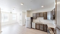 This 2-bedroom, 2-bathroom unit in Austin, TX offers a thoughtfully organized single-story layout with light wood-style flooring running throughout. The space features two separate kitchens, each equipped with dark-toned cabinetry, stainless steel appliances including a refrigerator and dishwasher, light granite-style countertops, and subway tile backsplashes. Recessed lighting and textured ceilings add dimension overhead. The living area is bright and open, benefiting from multiple windows fitted with horizontal blinds that allow natural light to filter in, complemented by a ceiling fan for year-round comfort. Both bedrooms are comfortably scaled, each with a ceiling fan, natural light from windows, and access to dedicated closets with built-in shelving. The bathrooms are cleanly finished, featuring dark vanity cabinetry with granite-style countertops and tiled tub-shower combinations. A convenient in-unit laundry area with washer and dryer hookups adds practicality. The overall palette is neutral and bright, with warm beige walls and white trim creating a clean, cohesive ambiance throughout.