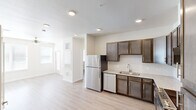 This 2-bedroom, 2-bathroom unit in Austin, TX offers a thoughtfully organized single-story layout with light wood-style flooring running throughout. The space features two separate kitchens, each equipped with dark-toned cabinetry, stainless steel appliances including a refrigerator and dishwasher, light granite-style countertops, and subway tile backsplashes. Recessed lighting and textured ceilings add dimension overhead. The living area is bright and open, benefiting from multiple windows fitted with horizontal blinds that allow natural light to filter in, complemented by a ceiling fan for year-round comfort. Both bedrooms are comfortably scaled, each with a ceiling fan, natural light from windows, and access to dedicated closets with built-in shelving. The bathrooms are cleanly finished, featuring dark vanity cabinetry with granite-style countertops and tiled tub-shower combinations. A convenient in-unit laundry area with washer and dryer hookups adds practicality. The overall palette is neutral and bright, with warm beige walls and white trim creating a clean, cohesive ambiance throughout.