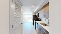 Located at 12729 Lake City Way NE in Seattle, WA, this efficiently designed unit offers a bright and modern living environment. The open-concept layout seamlessly connects the living area to a well-appointed kitchen, which features warm wood cabinetry, stainless steel appliances including a refrigerator, range, and microwave, as well as recessed lighting that keeps the space feeling fresh and functional.

Light hardwood flooring runs throughout the main living area, complementing the clean white walls and dark baseboards that define the contemporary aesthetic. A standout feature of the living space is the expansive picture window that frames sweeping views of the surrounding Seattle neighborhood and lush tree canopy beyond — flooding the interior with abundant natural light.

The bathroom is finished to a modern standard, showcasing a wood-toned vanity with an undermount sink, white quartz countertop, a large mirror, and chrome fixtures. The neutral tones and clean lines carry the cohesive design language of the rest of the unit.

The space also includes a private entry door, in-unit utility connections, and a layout that maximizes every square foot. Overall, the unit offers a crisp, move-in-ready environment with thoughtful finishes suited to contemporary urban living in the Lake City corridor of Seattle.