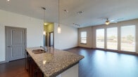 Located at 1350 N Greenville Ave in Richardson, Texas, this single-floor residence offers a well-designed open-concept layout that seamlessly integrates the kitchen, dining, and living areas. Rich dark hardwood flooring flows throughout the main living spaces, creating a warm and cohesive aesthetic.

The kitchen is a standout feature, appointed with dark espresso cabinetry, granite countertops, a white subway tile backsplash, and a full suite of stainless steel appliances including an electric range, microwave, and refrigerator. A large kitchen island with an undermount sink and elegant pendant lighting serves as the centerpiece, providing both functionality and style.

The spacious living area benefits from a bank of large windows that invite abundant natural light and offer views of the surrounding neighborhood. A ceiling fan adds comfort to the open room, while track lighting provides additional illumination.

The bedroom features plush carpeting, a natural light-filled window, and access to a well-appointed bathroom. The bathroom is finished with granite countertops, dark cabinetry, a large framed mirror, a walk-in shower, and hardwood-style flooring, with an adjacent walk-in closet offering ample storage. The overall ambiance is modern and move-in ready.