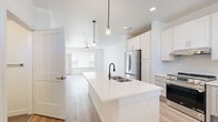 This single-story, 3-bedroom, 2-bathroom home offers a clean, modern aesthetic throughout, highlighted by a bright white color palette and light wood-look flooring in the main living areas. The open-concept kitchen is a standout feature, anchored by a large center island with a white quartz countertop, a deep dual-basin sink with a matte black faucet, and pendant lighting overhead. White shaker-style cabinetry lines the walls, complemented by stainless steel appliances including a refrigerator and range. The kitchen flows seamlessly into the living area, which features a ceiling fan and large windows that invite abundant natural light. The three bedrooms are carpeted for comfort, each with a ceiling fan and natural light from well-placed windows. The primary bedroom includes a sliding glass door opening to an outdoor balcony with exterior views, as well as a closet with double hanging rods. The two bathrooms are finished with large-format tile flooring and white vanities with quartz countertops. One bathroom features a glass-enclosed walk-in shower, while the other offers a shower-tub combination. A dedicated interior laundry room houses a full-size front-load washer and dryer. A hallway connects the home's rooms efficiently, completing this functional and thoughtfully designed layout.