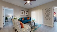 This single-floor residence offers a thoughtfully designed layout that balances comfort and functionality throughout. The living room serves as the heart of the home, showcasing light wood-style flooring, a ceiling fan, and large sliding glass doors dressed with vertical blinds that invite abundant natural light. The space is accented by warm neutral walls, creating a welcoming atmosphere.

The kitchen features white shaker cabinetry, a peninsula with a white countertop and undermount sink, and stainless steel appliances including a refrigerator, microwave, and range. Bright overhead lighting enhances the clean, modern aesthetic.

The primary bedroom is a serene retreat with a ceiling fan, large windows with blinds, and light wood-style flooring. An adjacent walk-in closet provides generous storage with multi-level hanging rails and a tufted bench. The full bathroom offers a white vanity with ample counter space, an undermount sink, and a bathtub with tile surround.

A second bedroom is configured as a creative, playful space with natural light and room to personalize. The in-unit laundry area houses a full-size washer and dryer alongside an electrical panel, offering added convenience. Throughout, the consistent use of light tones and wood-style flooring ties each room together cohesively.