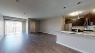 Located at 2760 S Highland Ave in Lombard, Illinois, this single-floor residence offers a thoughtfully designed open-concept layout that seamlessly connects the living, dining, and kitchen areas. Rich dark hardwood-style flooring runs throughout the main living space, complementing the neutral gray walls and creating a warm, contemporary ambiance.

The kitchen is a standout feature, showcasing dark espresso cabinetry with sleek bar-pull hardware, granite countertops, a classic subway tile backsplash, and a full suite of stainless steel appliances including a gas range, microwave, refrigerator, and dishwasher. A peninsula with pendant lighting provides an ideal breakfast bar and additional prep space.

The primary bedroom is generously sized with plush carpeting and direct access to a private en-suite bathroom. The en-suite includes a dark-toned vanity with a white countertop, a soaking tub, and a separate walk-in shower. A second bedroom, also carpeted with a sliding closet, is served by a well-finished second bathroom featuring a matching dark vanity and wood-look tile flooring. The open living area benefits from natural light and offers access to a balcony, enhancing the overall sense of space and connectivity to the outdoors.